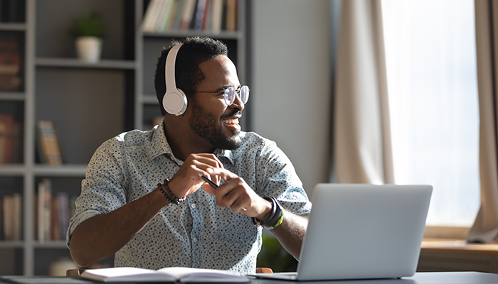 Happy relaxed millennial afro american business man wear wireless headphones look away rest at workplace finished work listening music podcast feel peace of mind concept sit at desk in sunny office