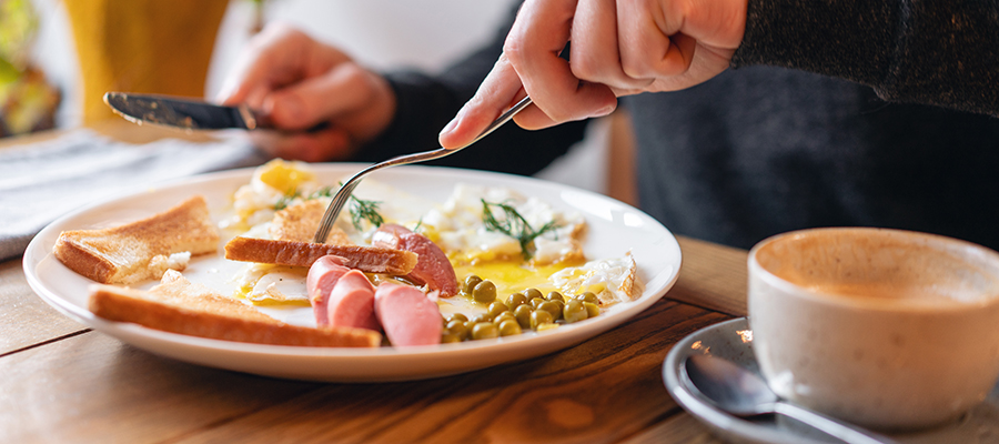 Person eating American style breakfast with fried eggs, sausage, green peas and toast. The concept of a healthy morning.