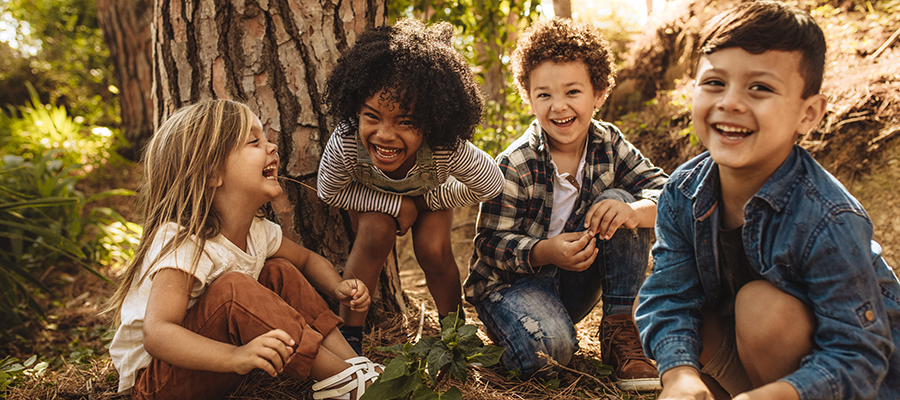 Group of cute kids sitting together in forest and looking at camera. Cute children playing in woods.